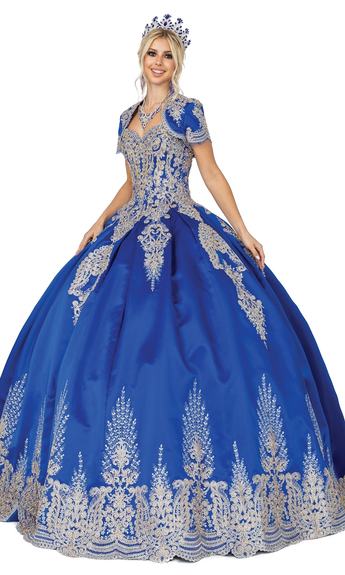 Woman stands smiling in the Quinceanera Dress 1494 by Dancing Queen—a royal blue A-line ball gown with intricate lace embroidery—paired with a matching tiara.